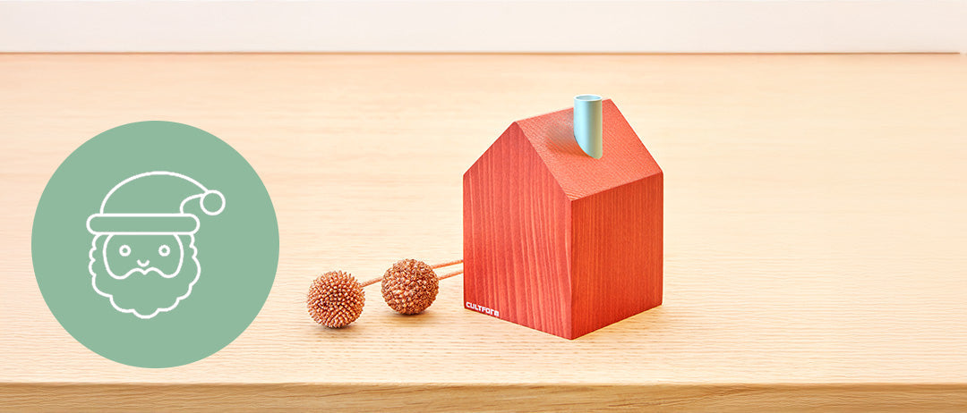 Vase mit roten Tulpen auf einem Holzlattentisch in einem hellen Wohnzimmer mit gestapeltem Brennholz und einem Kamin. Links ein Symbol mit Stühlen, einem Tisch und Sprechblasen auf einem grünen Kreis.