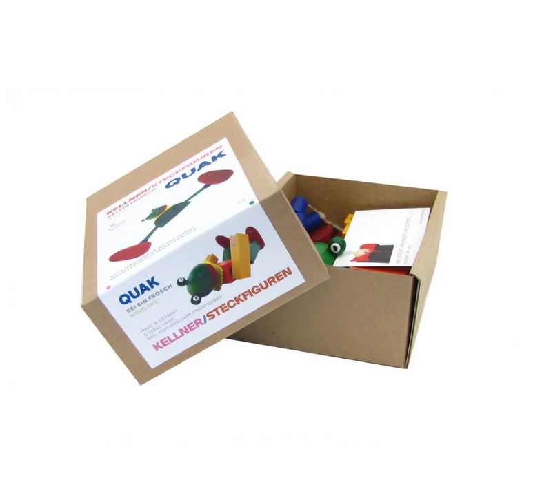 Eine braune Pappschachtel, die teilweise geöffnet ist, um farbenfrohes Holzspielzeug und eine Anleitung zu enthüllen, zeigt eine Illustration und einen Text für das Spielzeug "Frosch Quak - Kellner Steckfigur (Kopie)" von buchenblau mit der verspielten Figur Frosch Quak.