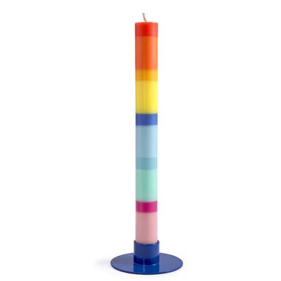 Eine hohe, zylindrische „Grußkerze Schulkind“ (nicht das Mädchen), aus Stearinwachs mit horizontalen Regenbogenschichten, steht auf einem runden blauen Sockel vor einem weißen Hintergrund.