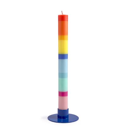 Eine hohe, zylindrische „Grußkerze Schulkind“ (nicht das Mädchen), aus Stearinwachs mit horizontalen Regenbogenschichten, steht auf einem runden blauen Sockel vor einem weißen Hintergrund.