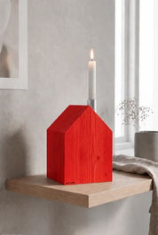 Ein leuchtend roter Kerzenhalter im Erzgebirgsstil („Großes Kerzenhaus“) mit einer einzelnen weißen Stumpenkerze, ausgestellt auf einem hölzernen Wandregal.