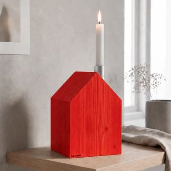 Ein leuchtend roter Kerzenhalter im Erzgebirgsstil („Großes Kerzenhaus“) mit einer einzelnen weißen Stumpenkerze, ausgestellt auf einem hölzernen Wandregal.