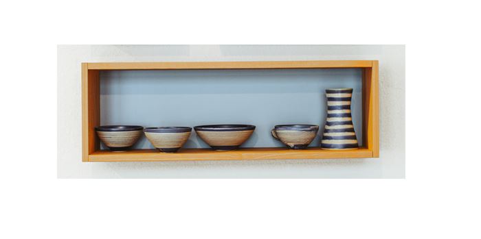 Der Wandregalwürfel Esche - L von buchenblau präsentiert wunderschön vier kleine Keramikschalen und eine blau-weiß gestreifte Vase mit seinem natürlichen Eschenholz-Finish vor dem charakteristischen buchenblau-Hintergrund der Marke.