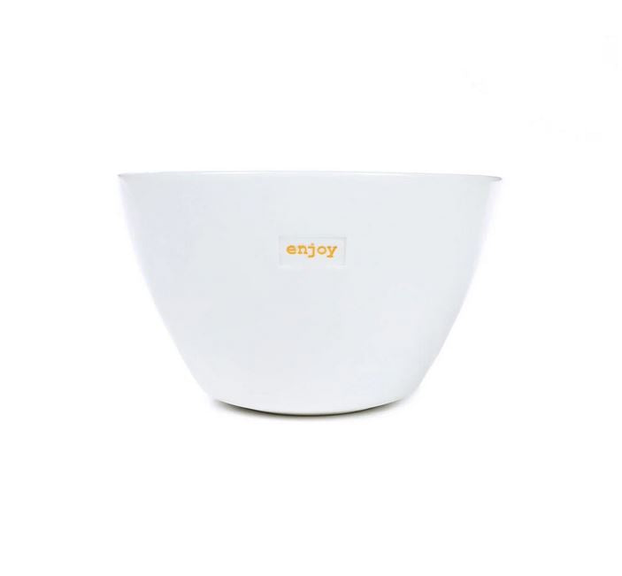 Die Schale „Enjoy“ von Keith Brymer Jones ist eine schlichte weiße Schüssel mit einem kleinen gelben Etikett auf der Vorderseite, auf dem „Enjoy“ in Kleinbuchstaben auf weißem Hintergrund steht.