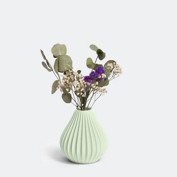 Die Vase „Raindrop“ in Salbei von nevalu besticht durch ein hellgrünes, geripptes Design und präsentiert ein wunderschönes Arrangement aus Eukalyptusblättern, Schleierkraut und violetten Blüten vor einem hellen Hintergrund. Dieses Stück ist ein Beispiel für nachhaltiges Design durch die Verwendung von recyceltem Kunststoff.