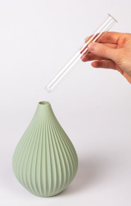 Eine Hand hält ein transparentes Reagenzglas über einer hellgrünen, gerippten Keramikvase „Raindrop“ in Salbei mit schmalem Hals von Nevalu vor einem schlichten weißen Hintergrund und zeigt nachhaltiges Design, das Tradition und Moderne elegant miteinander verbindet.