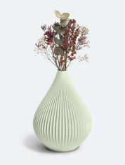 Eine hellgrüne, gerippte Vase „Raindrop“ von nevalu, hergestellt aus recyceltem Kunststoff, enthält ein zartes Arrangement aus getrockneten Blumen, darunter Lavendelzweige, Eukalyptusblätter und Schleierkrautbüschel, und schafft so eine minimalistische und elegante Präsentation vor einem schlichten Hintergrund.