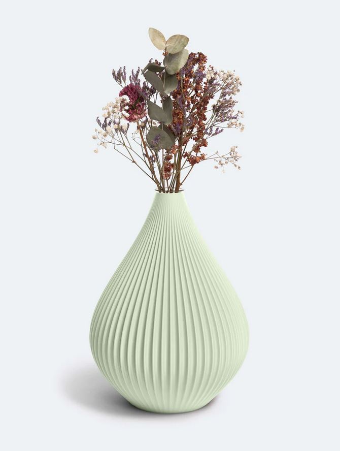 Eine hellgrüne, gerippte Vase „Raindrop“ von nevalu, hergestellt aus recyceltem Kunststoff, enthält ein zartes Arrangement aus getrockneten Blumen, darunter Lavendelzweige, Eukalyptusblätter und Schleierkrautbüschel, und schafft so eine minimalistische und elegante Präsentation vor einem schlichten Hintergrund.
