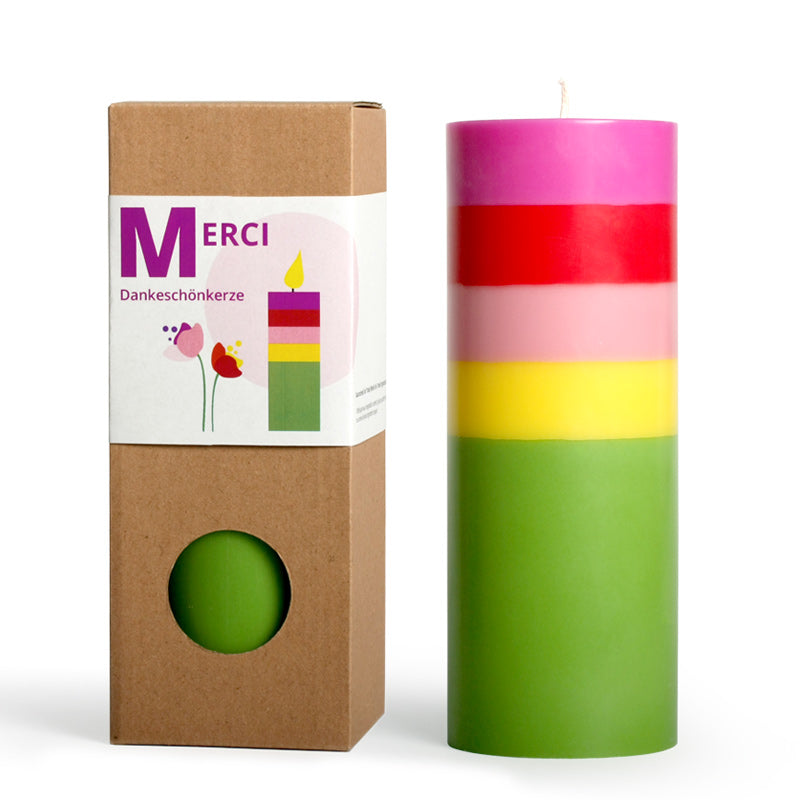 Die Große Kerze Merci von not the girl ist eine große, bunte Kerze aus Stearin-Wachs mit grünen, gelben, rosa und roten Schichten. Sie wird in einer braunen Schachtel geliefert, auf der eine Illustration der Kerze und das Wort "Merci" abgebildet sind.