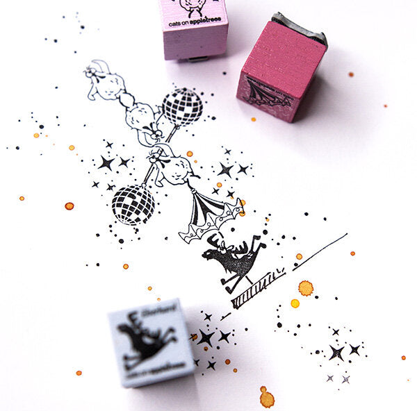 Eine skurrile Tuscheillustration zeigt Akrobaten auf Discokugeln, mit Stern- und Punktmustern. Daneben sind drei buchenblaue Ministempel - Adventskalender - zwei rosa und ein blauer - auf dem weißen Papier platziert.