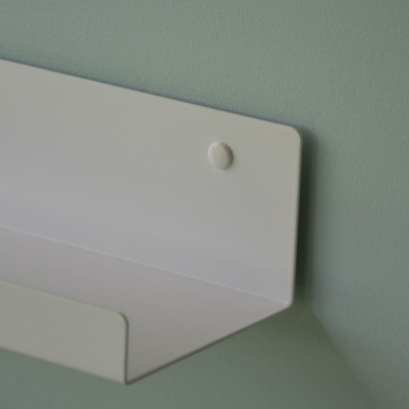 Eine Nahaufnahme des minimalistischen Wandregals Jill von Jan Kurtz, aus weißem Stahlrohr gefertigt und mit einem sichtbaren, abgerundeten Verschluss an einer hellgrünen Wand montiert – ein schlankes, modernes Design.