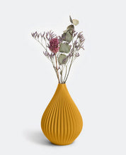 Ein kleines Arrangement aus Trockenblumen, darunter violette Zweige und Eukalyptusblätter, wird in einer senfgelben Keramikvase „Raindrop“ in Ocker von nevalu vor einem grauen Hintergrund präsentiert.