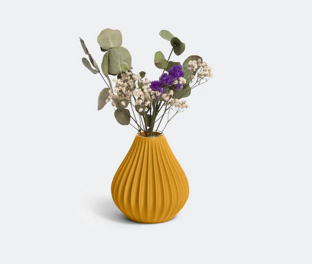 Die Vase „Raindrop“ in Ocker von nevalu, ein leuchtend gelbes geripptes Keramikstück, enthält ein atemberaubendes Arrangement aus getrockneten Blumen, darunter hellgrüne Eukalyptusblätter, zartes weißes Schleierkraut und einige violette Strandfliederblüten. Die Vase steht vor einem schlichten weißen Hintergrund.