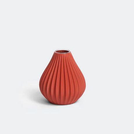 Die nevalu Vase „Raindrop“ in Terrakotta ist ein kleines, rundes Keramikstück mit schmaler Öffnung und geripptem, vertikalem Muster. Diese Vase aus recyceltem Kunststoff hat eine matte Oberfläche und steht vor einem schlichten weißen Hintergrund, was ihr nachhaltiges Design unterstreicht.